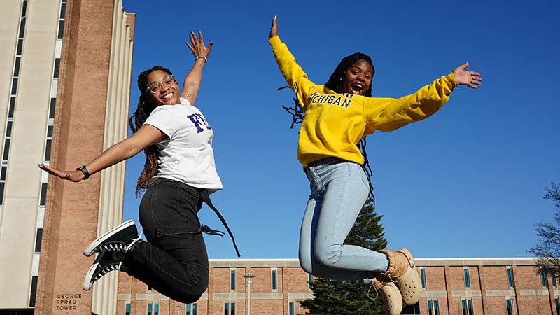 Two female students jumping outside SPRAU